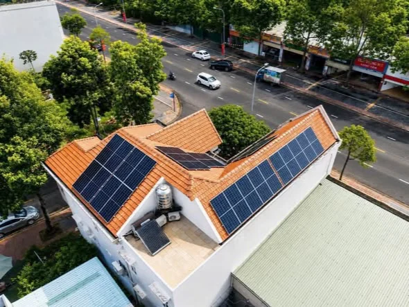 Các mảng tấm pin trên hai mặt mái ngói màu cam, cạnh khoảng sân đặt thiết bị nước nóng của nhà anh Trinh.